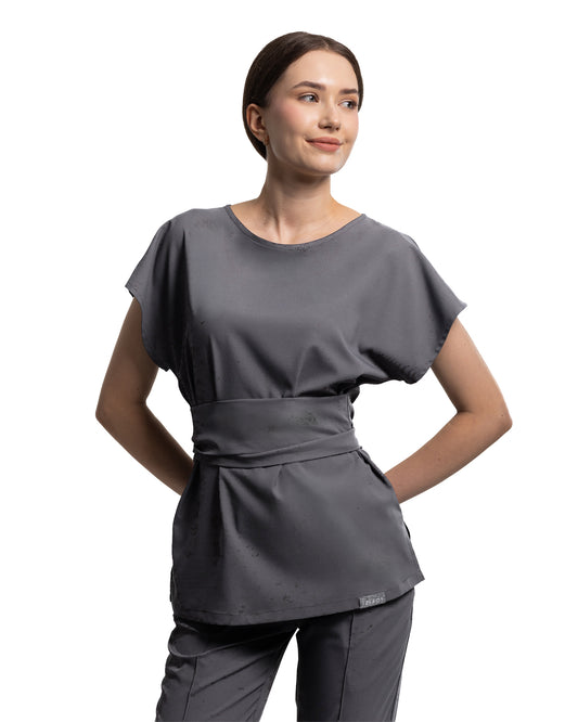 Femeie purtând bluza medicală CELESTE grafit cu centură și mânecă scurtă, culoare gri închis.